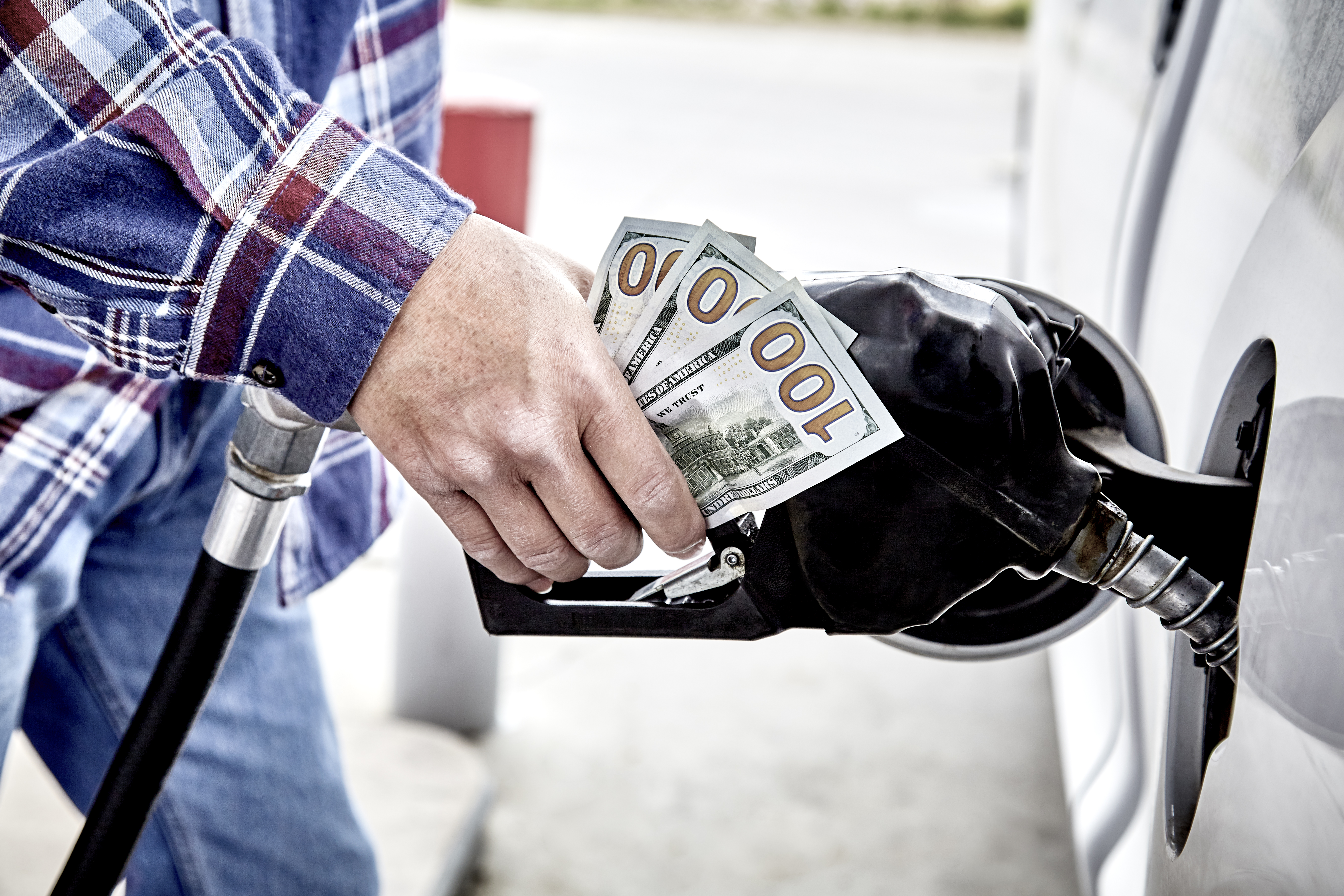 Close up of a person's hand on a gas dispenser nozzle clutching three United States one hundred dollar bills.