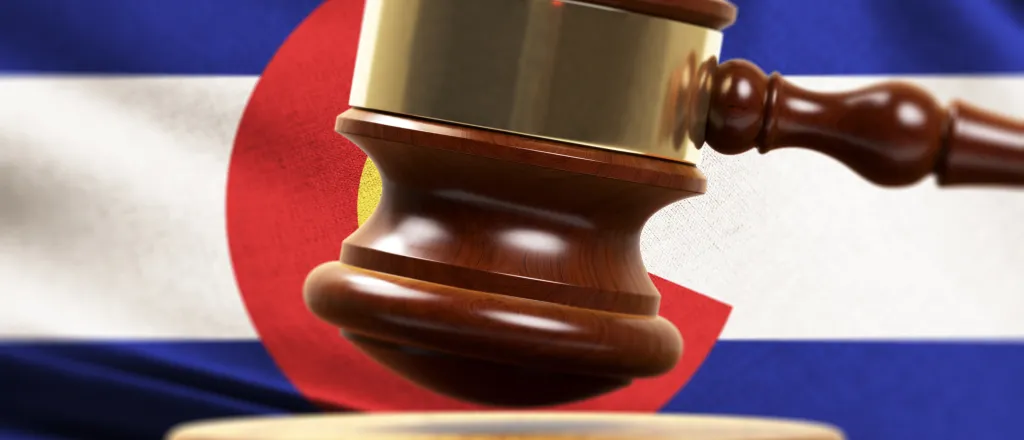 Gavel on a strike plate in front of the Colorado state flag.