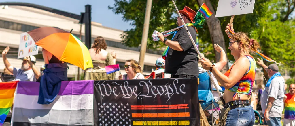 People marching in a pride parade with various flags and symbols.