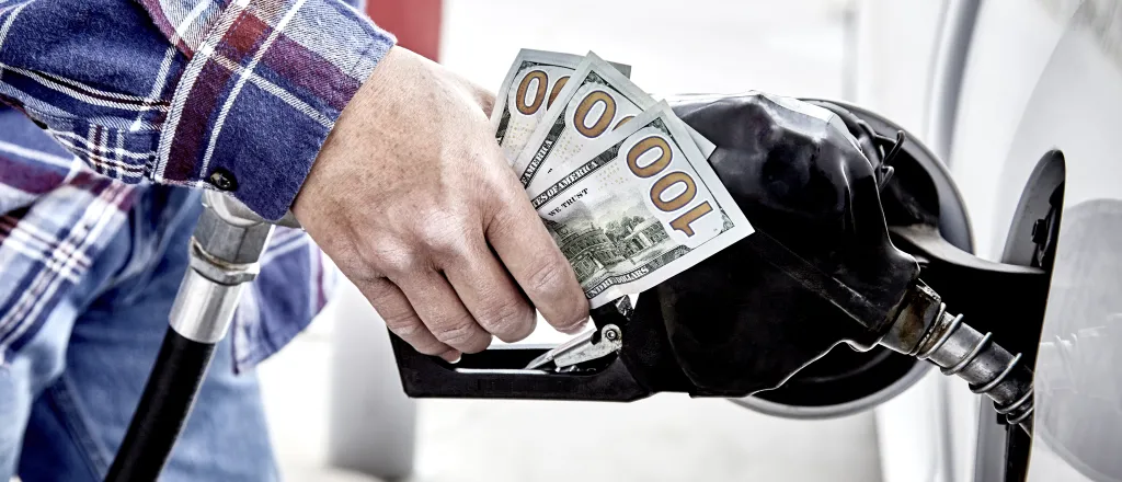 Close up of a person's hand on a gas dispenser nozzle clutching three United States one hundred dollar bills.