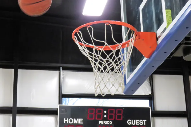 Basketball in the air approaching a basket. A scoreboard is in the background.
