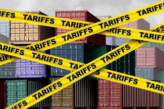 Artist's representation of cargo shipping containers with yellow banners in front labeled with the word "tariff"