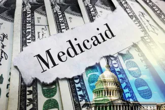 A scrap of torn paper with the word "Medicaid" rests on top of a spread of United States 100 dollar currency.
